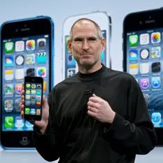 Steve Jobs prezentuje iPhone'a na tle rzędu smartfonów.