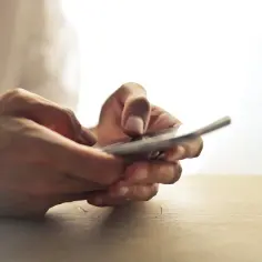 Dłonie trzymające smartfon i piszące na ekranie.