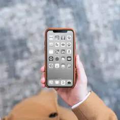Dłoń trzyma iPhone'a z czarno-białym ekranem i ikonami aplikacji.