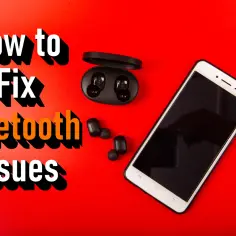 Jak naprawić problemy z Bluetooth na iPhone? Na czerwonym tle leży smartfon, słuchawki bezprzewodowe i etui ładujące.