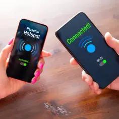Dwie dłonie trzymają telefony. Na jednym ekranie "Personal Hotspot Activated...", na drugim "Connected! Wi-Fi". Pokazuje, jak udostępnić Wi-Fi iPhone.