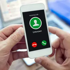 Dłoń trzyma smartfon z ekranem "Incoming Call... Unknown". Zastanawiasz się, jak ukryć swój numer?