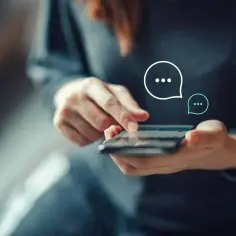 Dłonie trzymające smartfon, na ekranie widoczne ikony czatu. Zastanawiasz się, jak wysłać anonimowy SMS?