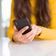 Kobieta w żółtym swetrze trzyma czarny telefon. Zastanawiasz się, co zrobić ze znalezionym telefonem?