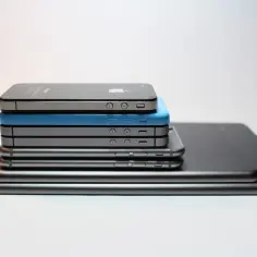 Stos różnych modeli iPhone'ów i iPadów na białym tle.