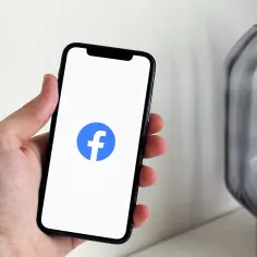 Dłoń trzyma smartfon z otwartą aplikacją Facebook.