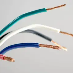 Kolorowe, stare kable elektryczne: zielony, biały, czarny, niebieski i różowy, z odsłoniętymi miedzianymi żyłami.