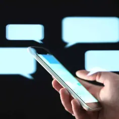 Dłoń trzymająca smartfon na tle dymków czatu.