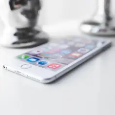 Biały iPhone na białym blacie, gotowy do uporządkowania. Ikony aplikacji, w tym Safari, są widoczne.