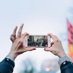 Dłonie trzymają iPhone'a w poziomie, nagrywając tłum. Dowiedz się, jak obrócić ekran w iPhone, by uchwycić szerszy kadr.