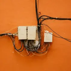 Skrzynki elektryczne na pomarańczowej ścianie, plątanina kabli. Widać, jak zrobić uziemienie w starej instalacji, choć wygląda to chaotycznie.