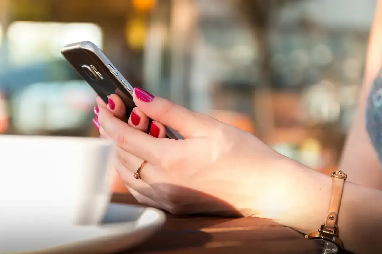 Dłoń z czerwonymi paznokciami trzyma telefon, obok biała filiżanka. Może to numer poczty głosowej Orange?