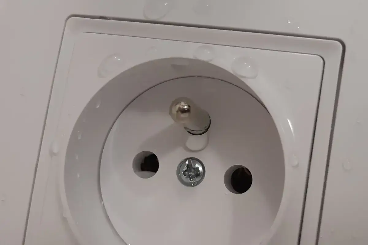 Bolec w gniazdku na górze czy na dole? Krople wody na białej ramce gniazdka elektrycznego.