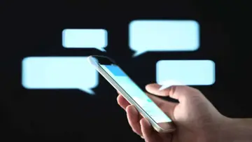Dłoń trzymająca smartfon na tle dymków czatu.