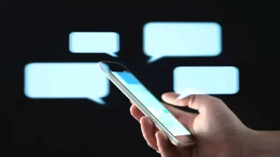 Dłoń trzymająca smartfon na tle dymków czatu.